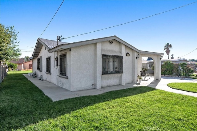 view of side of home with a lawn, a patio area, fence, and stucco siding