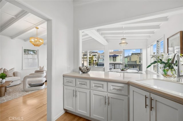 kitchen featuring lofted ceiling with beams, a sink, light countertops, hanging light fixtures, and light wood finished floors