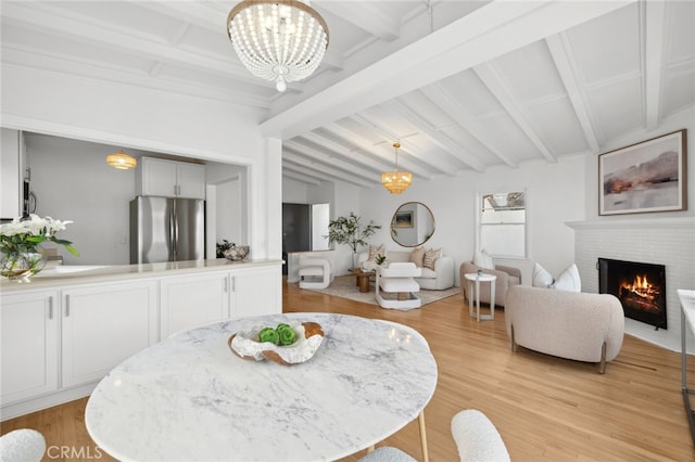 dining room with lofted ceiling with beams, a brick fireplace, light wood-style flooring, and a notable chandelier