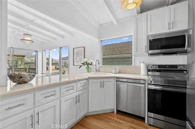 kitchen featuring beam ceiling, appliances with stainless steel finishes, light countertops, and a sink