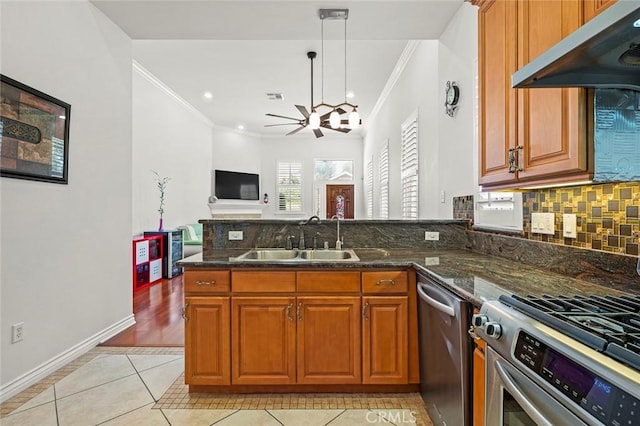 kitchen featuring under cabinet range hood, stainless steel appliances, a peninsula, a sink, and brown cabinetry