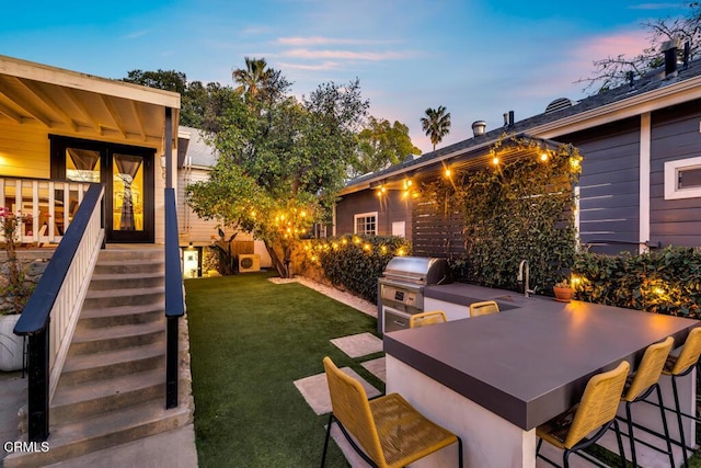 patio terrace at dusk featuring area for grilling, outdoor dry bar, grilling area, a yard, and a sink