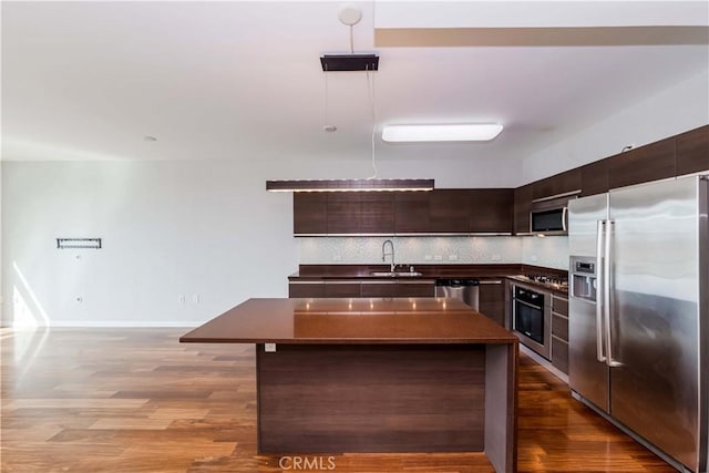 kitchen with dark countertops, decorative backsplash, appliances with stainless steel finishes, a sink, and dark brown cabinets