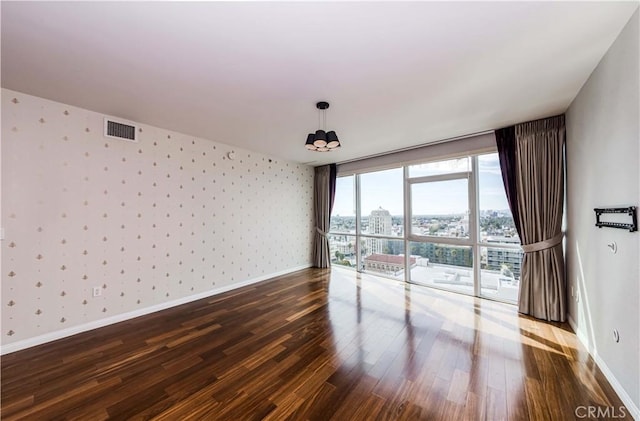 unfurnished room with dark wood-style floors, visible vents, baseboards, and wallpapered walls