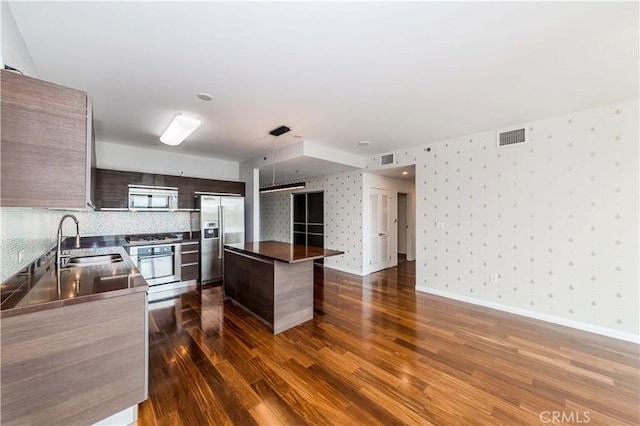 kitchen featuring stainless steel appliances, visible vents, a sink, modern cabinets, and wallpapered walls