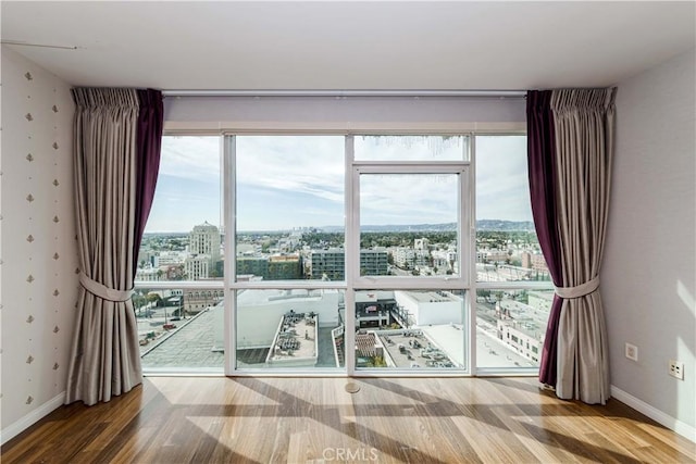 empty room with wallpapered walls, baseboards, a city view, and wood finished floors