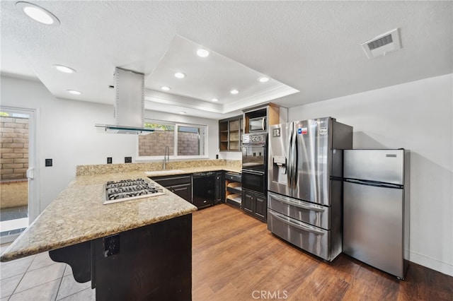 kitchen with a peninsula, visible vents, ventilation hood, black appliances, and a tray ceiling