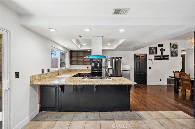 kitchen featuring a raised ceiling, visible vents, a sink, island range hood, and a peninsula