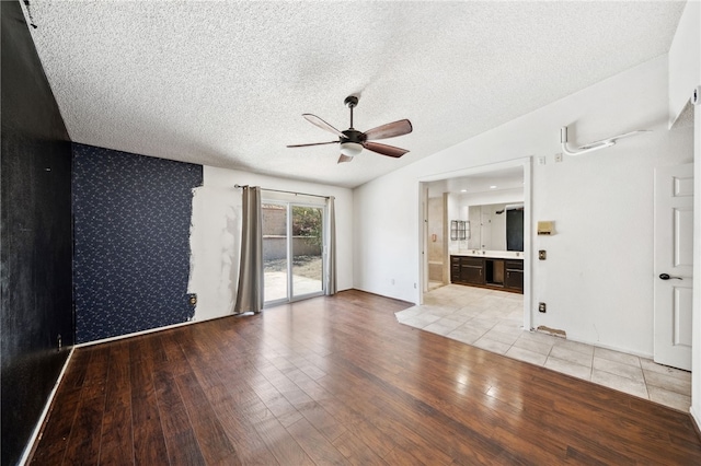 unfurnished living room with a ceiling fan, an accent wall, vaulted ceiling, a textured ceiling, and light wood-style floors