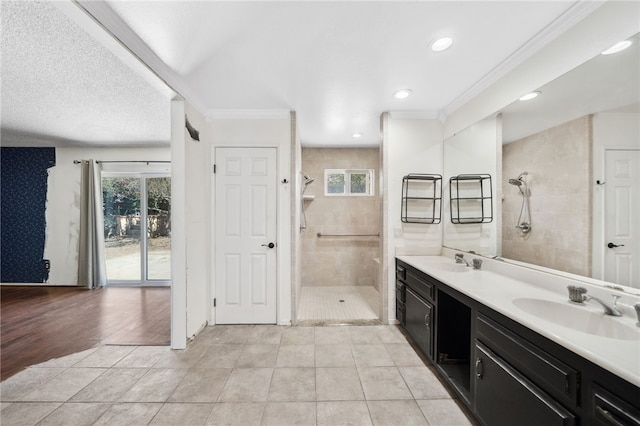 bathroom featuring ornamental molding, tile patterned flooring, tiled shower, and a sink