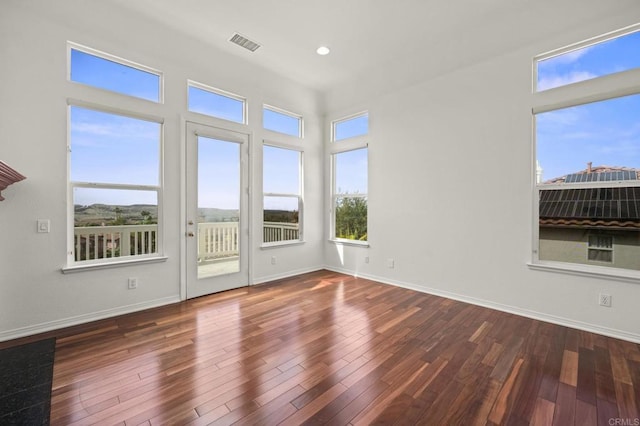 empty room with wood finished floors, visible vents, and baseboards