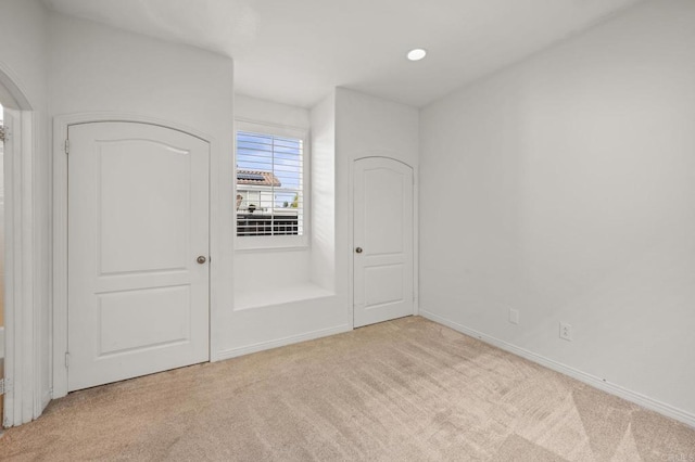 unfurnished bedroom with arched walkways, light colored carpet, baseboards, and recessed lighting