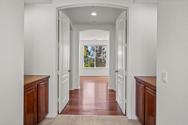 hall with light carpet, light wood-style flooring, and arched walkways