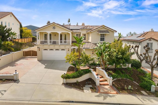 mediterranean / spanish home featuring stucco siding, solar panels, concrete driveway, fence, and a tiled roof