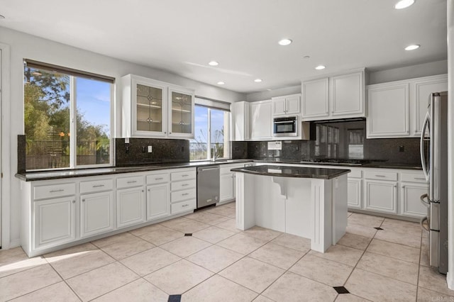 kitchen with light tile patterned flooring, stainless steel appliances, white cabinets, a center island, and tasteful backsplash