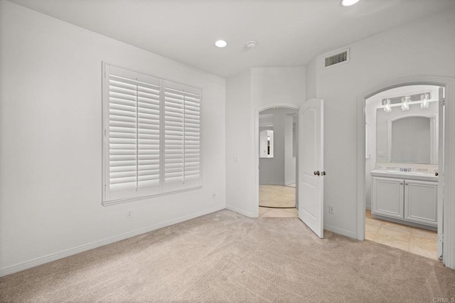 unfurnished bedroom with arched walkways, light carpet, visible vents, and recessed lighting