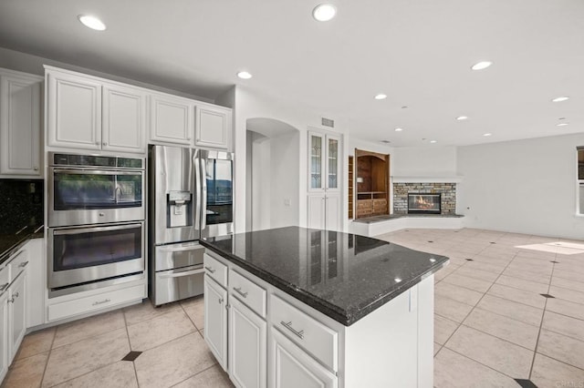 kitchen with light tile patterned floors, arched walkways, white cabinets, stainless steel appliances, and backsplash