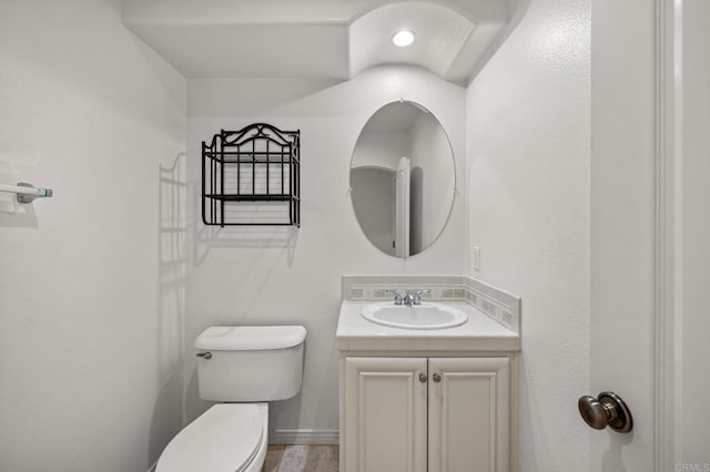 half bath with baseboards, vanity, and toilet