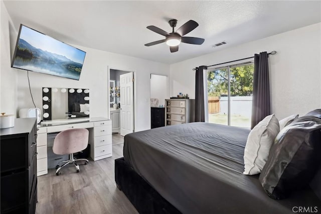 bedroom with access to exterior, visible vents, a ceiling fan, ensuite bath, and wood finished floors