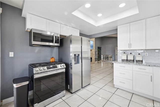 kitchen with white cabinets, appliances with stainless steel finishes, backsplash, and a tray ceiling