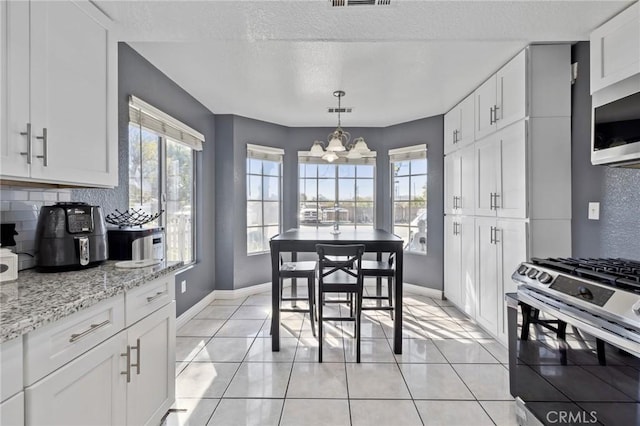 kitchen with stainless steel gas range, white cabinets, light tile patterned flooring, and decorative backsplash