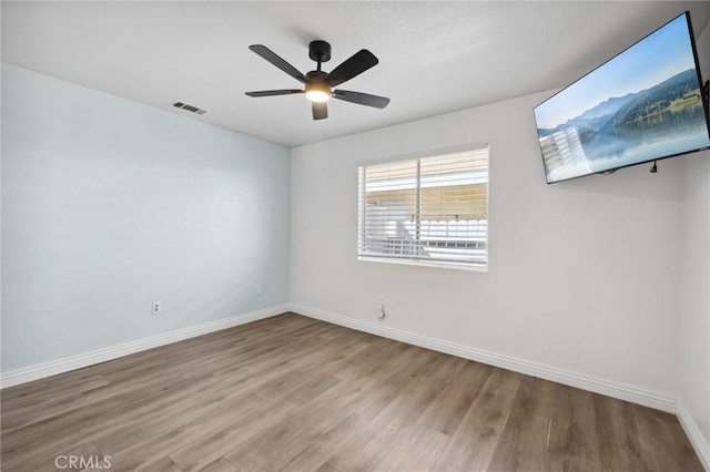 spare room featuring a ceiling fan, visible vents, baseboards, and wood finished floors