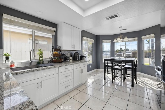 kitchen with a notable chandelier, visible vents, backsplash, white cabinetry, and a sink