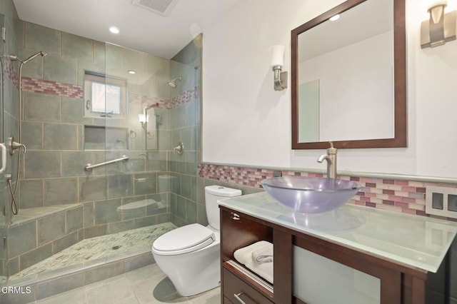 full bathroom with tile walls, visible vents, toilet, a tile shower, and vanity