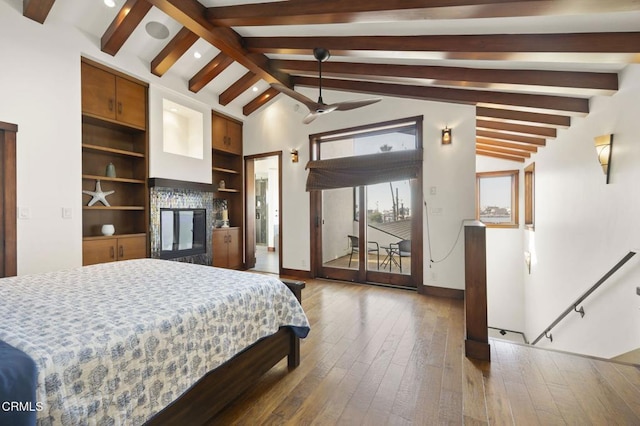 bedroom featuring baseboards, a glass covered fireplace, lofted ceiling with beams, hardwood / wood-style floors, and access to outside