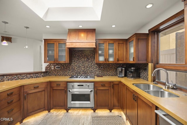 kitchen featuring stainless steel appliances, brown cabinetry, a sink, and custom exhaust hood