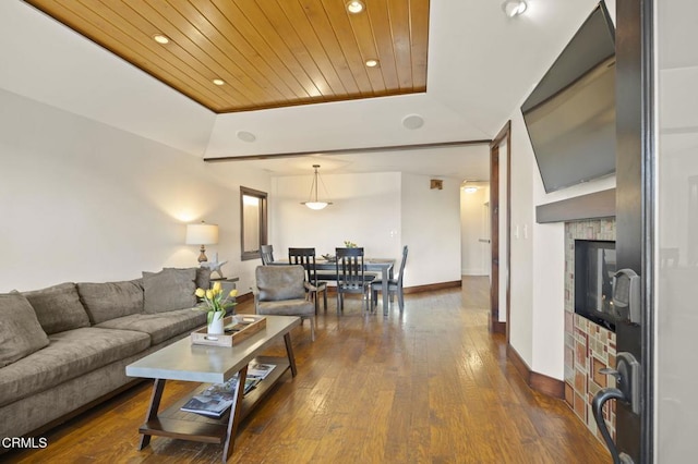 living room featuring a tray ceiling, a fireplace, dark wood finished floors, wooden ceiling, and baseboards