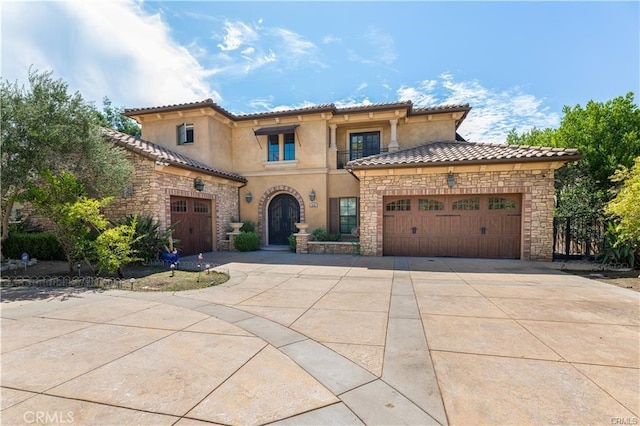 mediterranean / spanish house with an attached garage, a tile roof, driveway, stone siding, and stucco siding