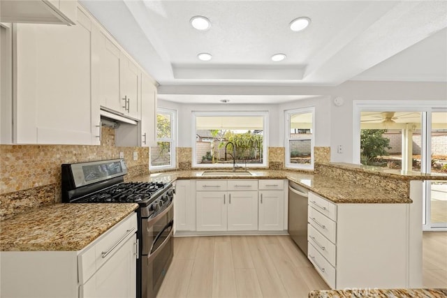 kitchen featuring light stone counters, a tray ceiling, appliances with stainless steel finishes, a sink, and a peninsula