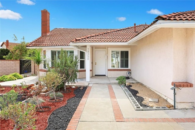 view of exterior entry with a tiled roof, a chimney, and stucco siding