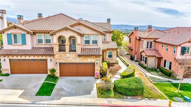 mediterranean / spanish house with an attached garage, a tile roof, driveway, stone siding, and stucco siding