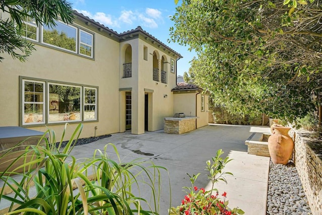 rear view of property featuring a tiled roof, stucco siding, and a patio area