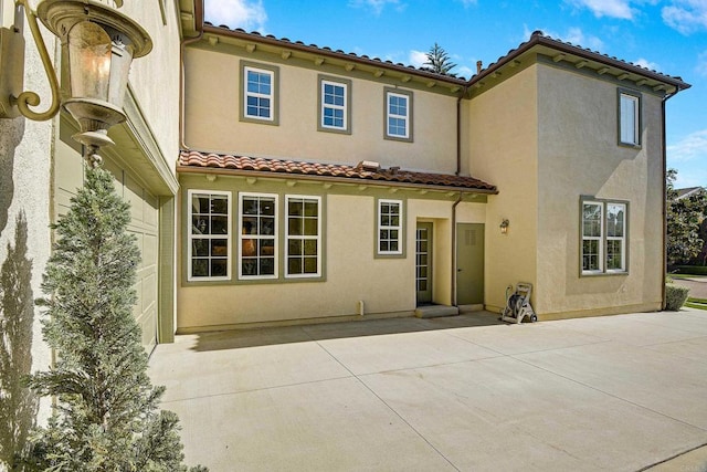 rear view of house with stucco siding, a tile roof, and a patio