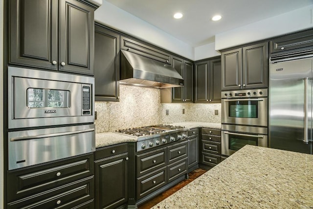 kitchen with backsplash, ventilation hood, light stone countertops, built in appliances, and a warming drawer