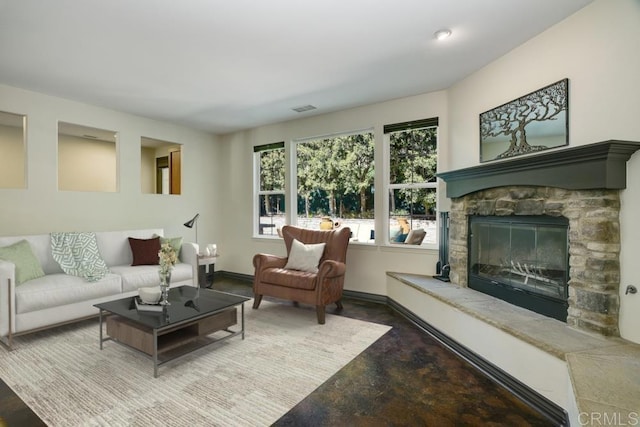 living area featuring a stone fireplace, visible vents, baseboards, and concrete flooring