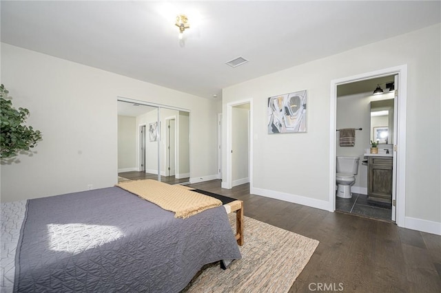 bedroom featuring wood finished floors, visible vents, baseboards, a closet, and ensuite bath