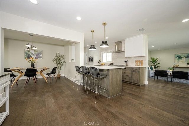 kitchen with a kitchen breakfast bar, dark wood-type flooring, light countertops, wall chimney range hood, and recessed lighting