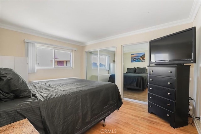 bedroom with crown molding, light wood finished floors, and two closets