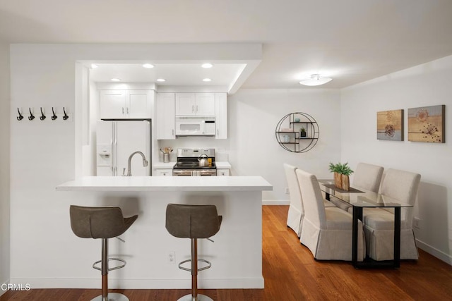 kitchen with white appliances, a breakfast bar area, a peninsula, light countertops, and a sink