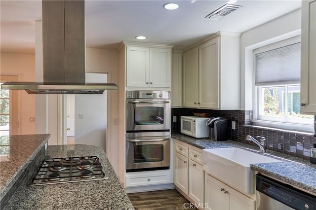 kitchen featuring stainless steel appliances, tasteful backsplash, visible vents, a sink, and island range hood