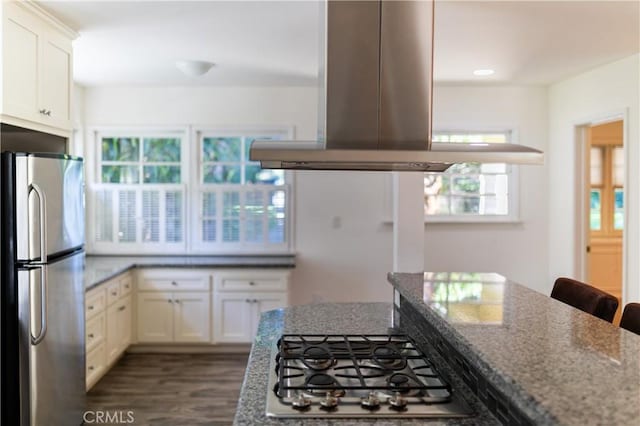 kitchen featuring island range hood, a kitchen breakfast bar, white cabinets, appliances with stainless steel finishes, and dark stone counters