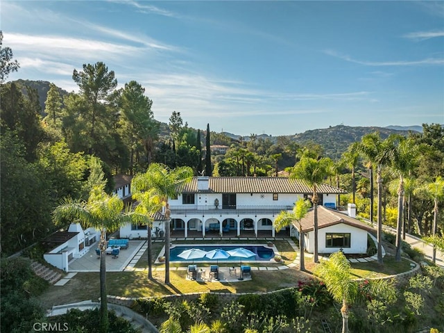 rear view of house featuring an outdoor pool, a jacuzzi, a patio area, a mountain view, and stucco siding