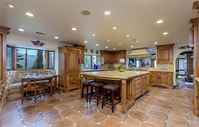 420 Inverness Dr, La Canada Flintridge, CA 91011 - kitchen with custom exhaust hood, a kitchen island, a breakfast bar area, brown cabinets, and a wealth of natural light