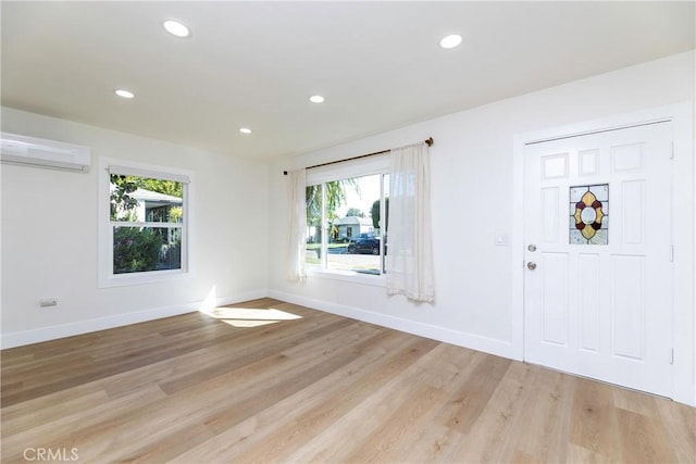 empty room with light wood-type flooring, a wall unit AC, and baseboards