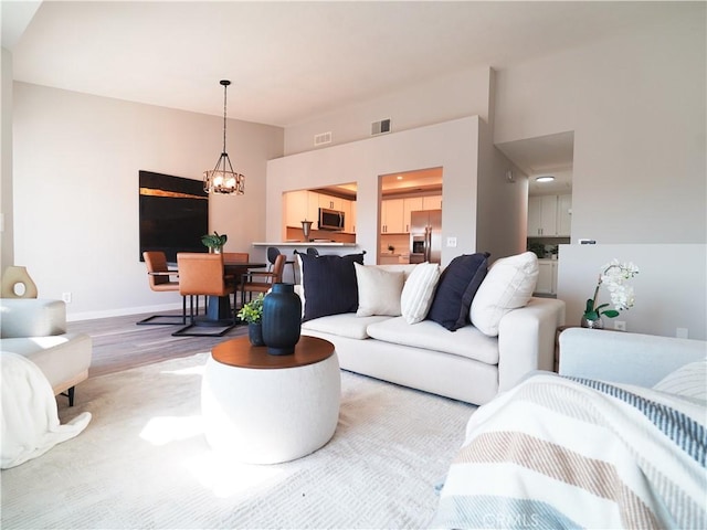 living area with a chandelier, wood finished floors, visible vents, and baseboards