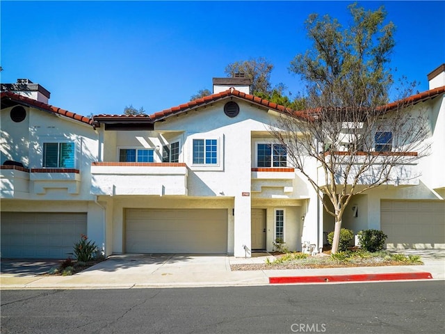 view of front facade featuring a tile roof, a chimney, stucco siding, concrete driveway, and an attached garage